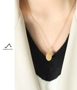 Polished oval gold pendant on a beaded stainless steel chain worn by a model