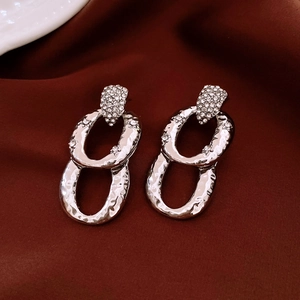 Close-up of silver interlocking earrings with zircons on dark red fabric background