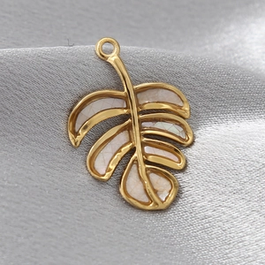 Macro detail of a golden monstera leaf pendant with natural white shell inlay on grey silk