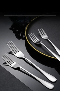 Close-up of mirror-polished stainless steel dinner and dessert forks on dark tableware