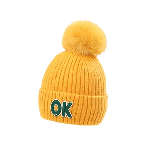 Bright yellow knitted children's beanie with a large faux fur pompom and OK patch