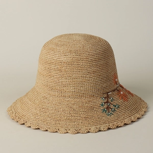 Close-up of hand-embroidered flowers and pearl beads on beige raffia cloche hat