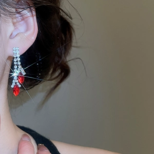 Close-up of sparkling ruby and diamond tassel earrings worn on ear with starburst light