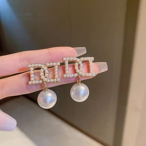 Detailed view of gold CD letter earrings with pavé pearls and hanging pearl drop
