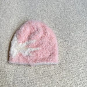 Detail of pink and white plush knit beanie with soft faux fur texture on a grey rug