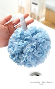 Close-up of a soft light blue mesh bath sponge with a branded hanging ribbon strap