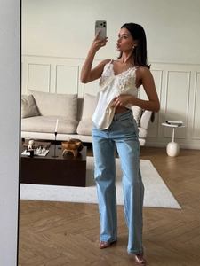 Détail d'un caraco blanc en dentelle et satin porté avec un jean large bleu clair