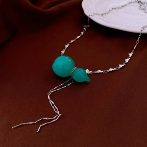 Detail of green gourd pendant and heart-shaped silver tassel chain on a brown fabric background