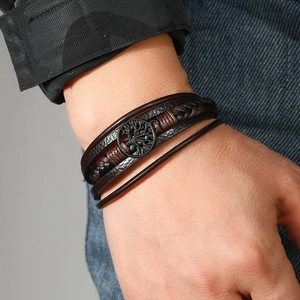 Detailed close-up of a multi-layer leather bracelet with tree of life charm on male wrist