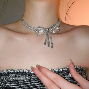 Close-up of bow necklace with sparkling crystals, pearls and tassels worn by a model