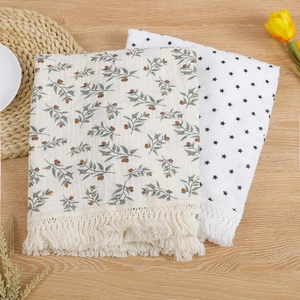Two cotton muslin baby blankets with fringe tassels featuring botanical and star prints