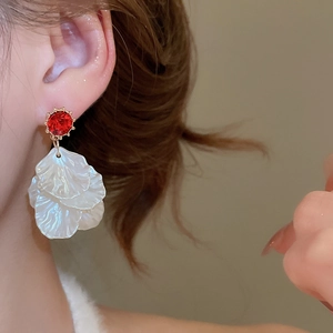 Detailed view of red rhinestone and white shell petal tassel earrings on a model
