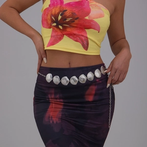 Detail of silver shell-shaped metal body chain worn over floral dress for beach style