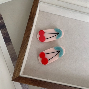 Detailed view of cherry-shaped acetate hair clips with red fruit and green leaves