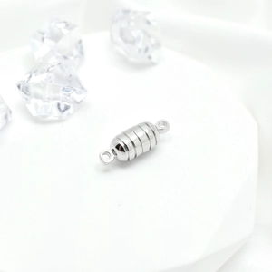 Polished silver cylindrical magnetic jewelry clasp on a white display stand for necklaces