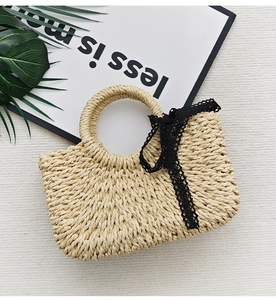 Close-up of woven straw handbag featuring black lace bow detail and natural fiber texture