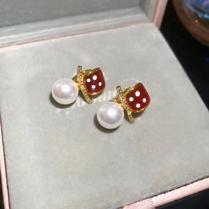 Macro shot of 18K gold plated pearl earrings with red dice and sparkling crystals