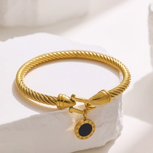 Close-up of gold twisted cable bangle featuring a black Roman numeral charm pendant