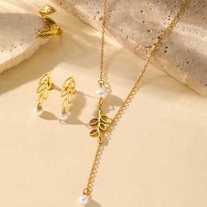 Flat lay of leaf-themed gold necklace, earrings and pearl ring set on natural stone