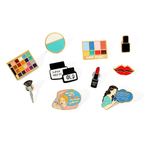 Detailed view of nine colorful enamel makeup themed pins with bold text on white background