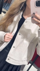 Detail of cream tweed varsity jacket with metallic snap buttons and textured fabric finish