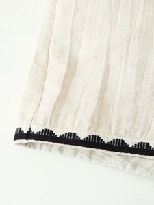 Close-up of beige cotton fabric with black wavy embroidery and pleated texture detail