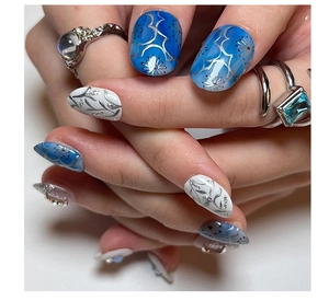 Macro shot of blue gradient press-on nails with silver floral patterns and tiny rhinestones