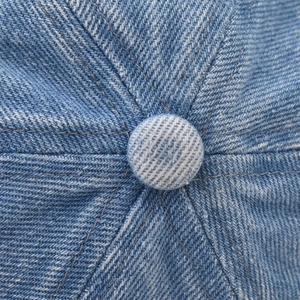 Macro detail of washed denim baseball cap top button and precision stitched seams