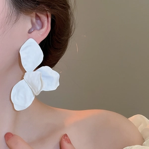 Close-up of elegant oversized white matte flower earrings worn by a female model