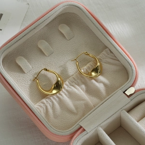 Macro shot of gold twisted hoop earrings inside a pink portable jewelry box