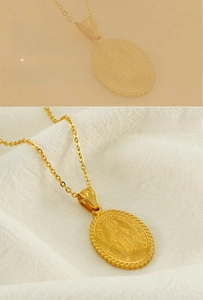 Macro shot of gold stainless steel oval Virgin Mary pendant necklace on white fabric