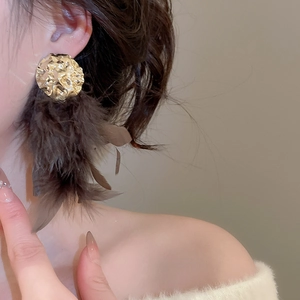 Macro shot of oversized gold hammered metal earrings with brown feather fringe details
