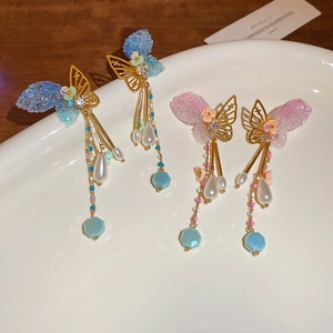 Detail of butterfly tassel earrings with blue and pink wings on a white ceramic tray