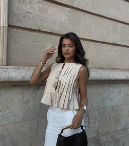 Detail of beige pleated sleeveless top with front tie strings and linen-like texture