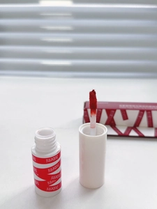 Detail of red matte lip mud with applicator brush and matching brand packaging box