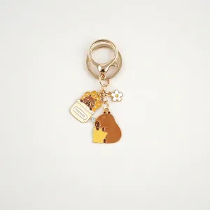 Detail of metal capybara keychain with enamel fries and flower charms on a golden ring