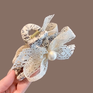 Détail d'une pince à cheveux avec nœud en dentelle, tissu floral et perle élégante