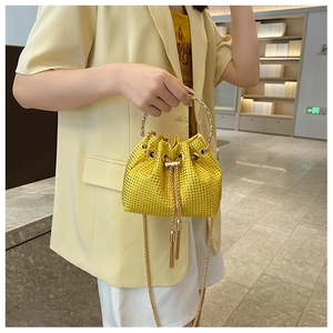 Close-up of sparkling yellow rhinestone bucket bag with metal chain and handle worn by model