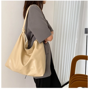 Model wearing a large beige leather tote bag with shoulder strap knot detail
