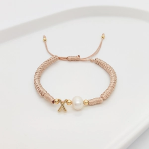 Detail view of woven bracelet with white pearl, letter X charm, and adjustable cord