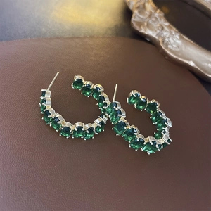 Detailed view of C-shape gold hoop earrings with green oval-cut crystal settings