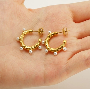 Detail view of 18K gold-plated C-shape earrings with hammered texture and pearls