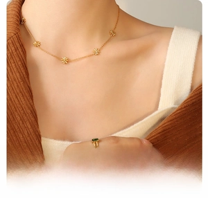 Detail of 18K gold-plated daisy necklace and green gemstone ring on titanium steel