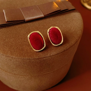 Close-up of golden oval earrings with red velvet texture on a brown gift box