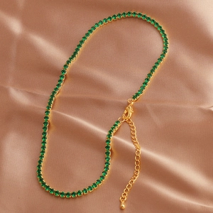 Macro view of emerald green tennis necklace with gold lobster clasp on satin fabric