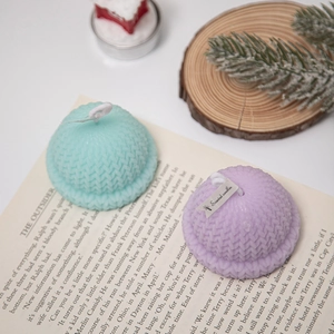 Knitted hat-shaped scented candles in mint and lilac on a rustic holiday book setting