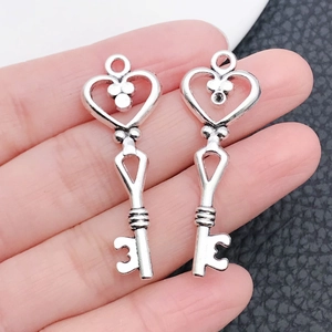 Detail of silver alloy heart skeleton key pendants held by hand to show the actual size