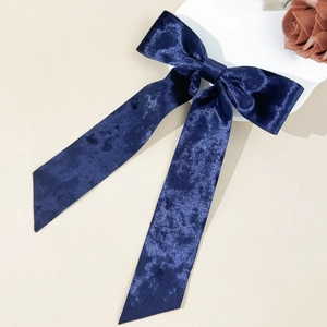 Detail of elegant dark blue velvet bow hair clip with long ribbons on beige background