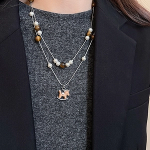 Détail du collier à deux rangs avec perles blanches, œil de tigre et pendentif cheval en bois