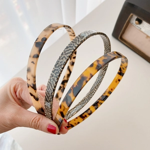 Hand holding four thin acetate headbands in tortoise shell and grey checkered patterns